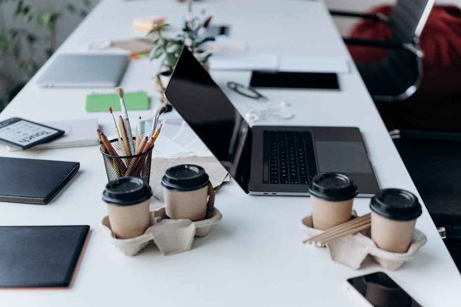 Multiple coffee cups arranged on a desk next to a laptop showing afternoon work fatigue