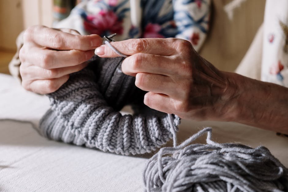 Hands knitting a soft grey scarf on bamboo needles in warm afternoon light