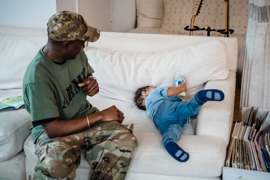 Soldier in uniform sitting on edge of bed at home looking distressed