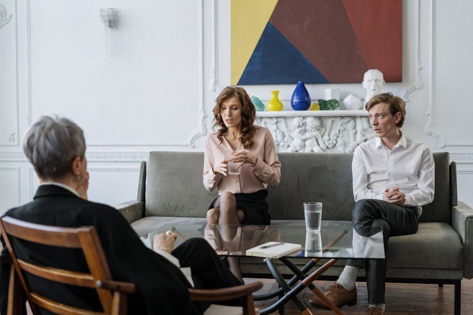 Couple sitting on couch in therapist office during sex therapy intake session with notebook