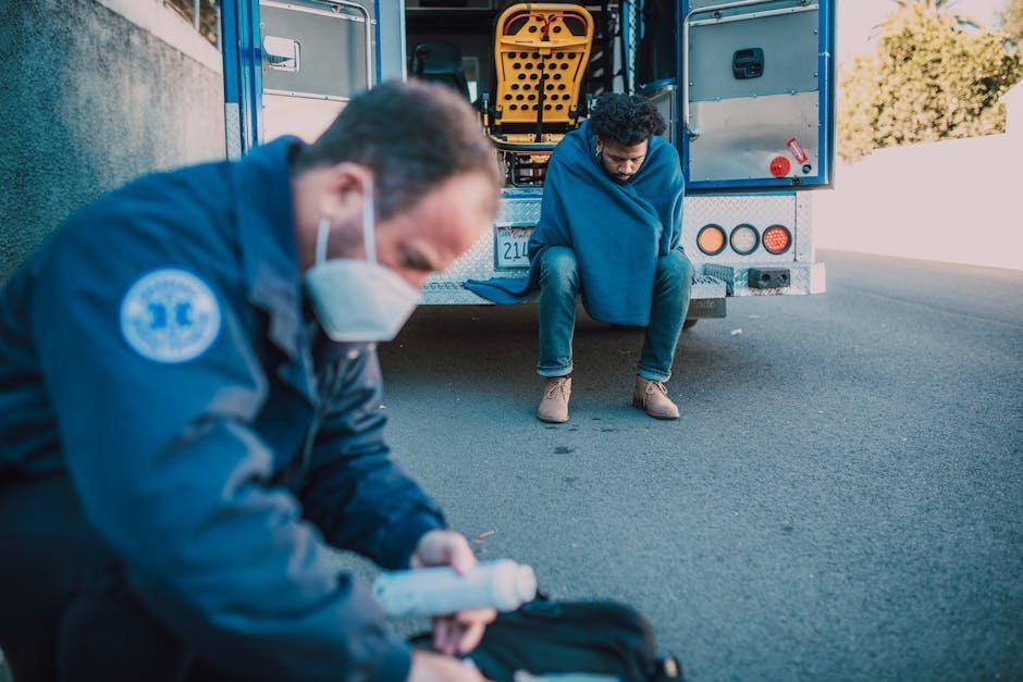 First responder sitting on the curb of a roadside scene with emergency vehicle lights in the background