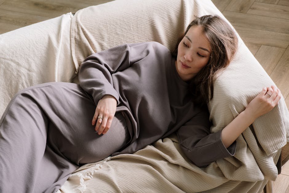 New mother resting on couch in fourth trimester with newborn nearby