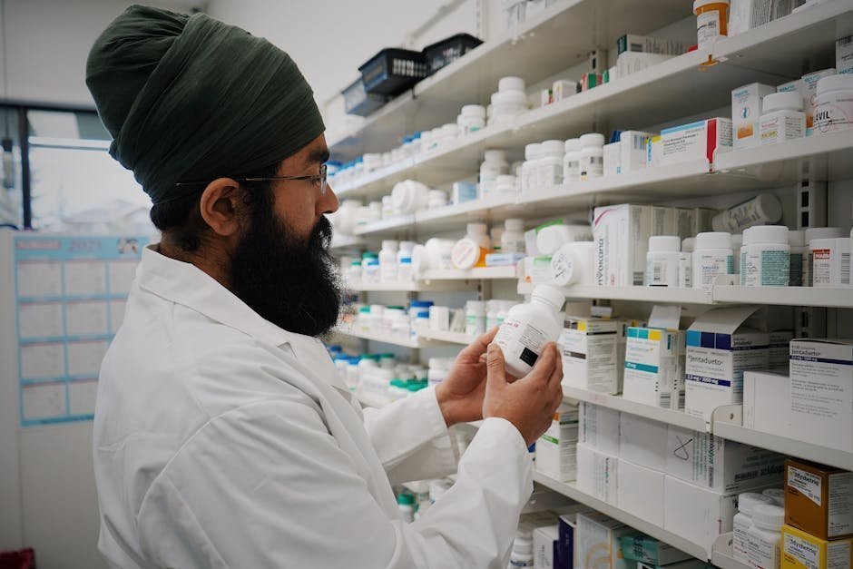 Pharmacist in white coat reviewing a prescription on a computer screen with sealed cold-chain shipping containers in the background