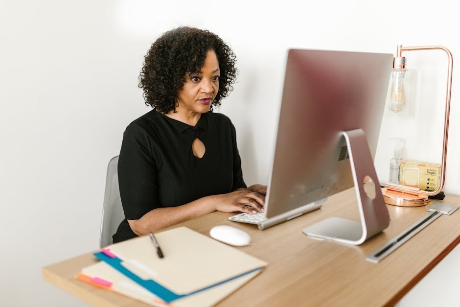 Mid-career professional sitting at home office desk reviewing career change notes and laptop, contemplative